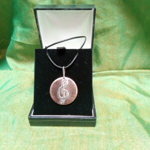 Handcrafted copper pendant with silver treble clef inlay using recycled materials